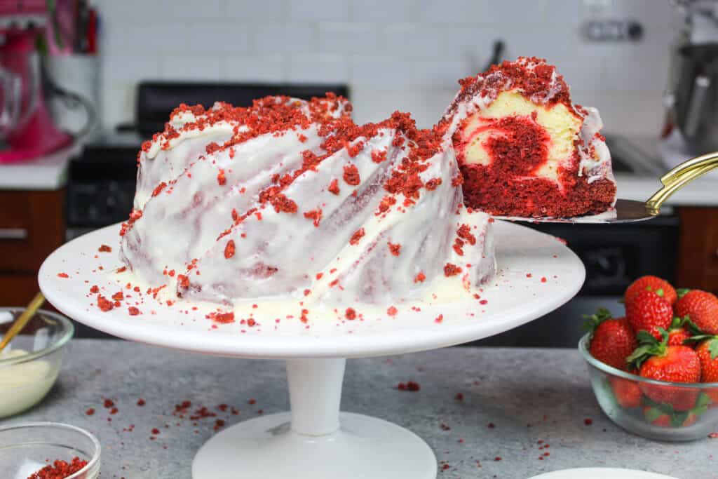 image of red velvet bundt cake recipe with slice being pulled out from the side, showing the cream cheese ripple that swirls through the middle of the bundt