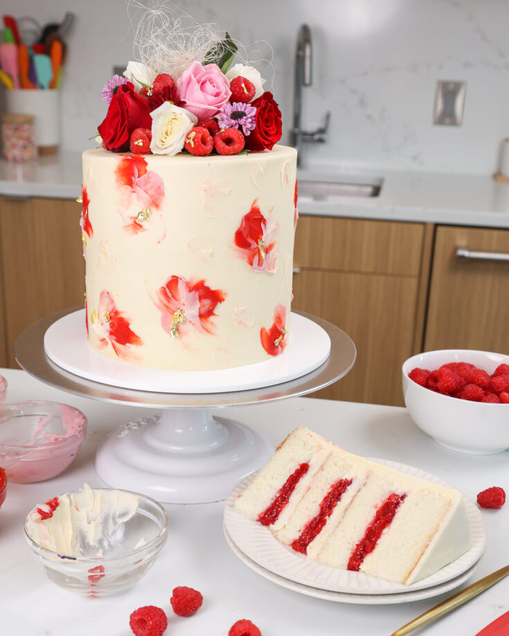 image of a white chocolate raspberry cake that is made with fluffy vanilla cake layers, tart raspberry cake filling, and white chocolate buttercream frosting