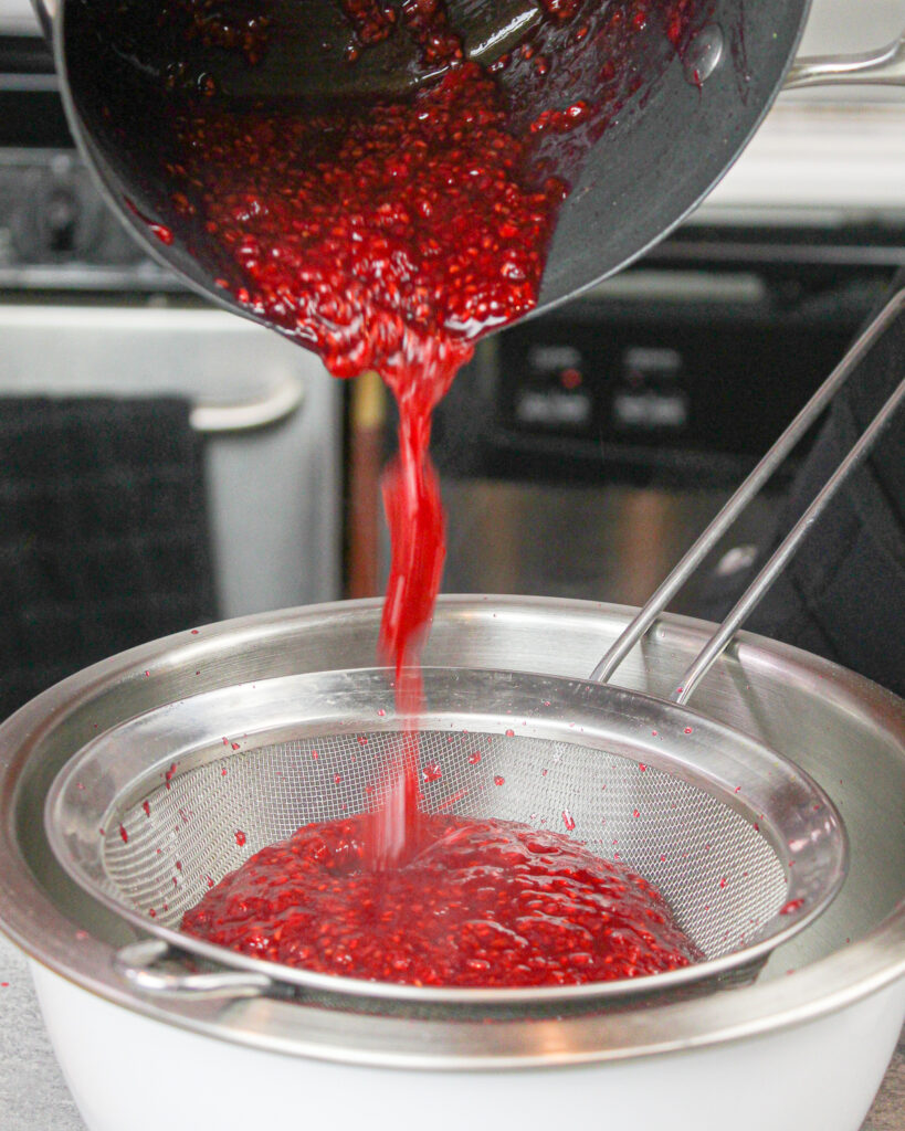 image of pouring raspberry compote through a strainer to make it seedless for a cake filling