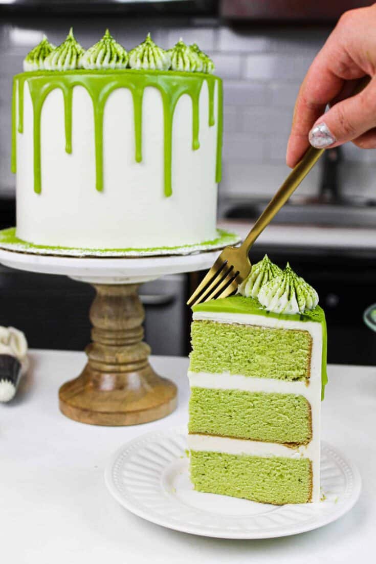 image of matcha cake slice on a plate with pretty matcha drip cake in background