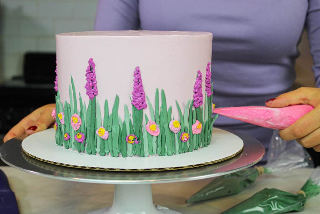 image of spring easter cake being decorated with lavender buttercream flowers
