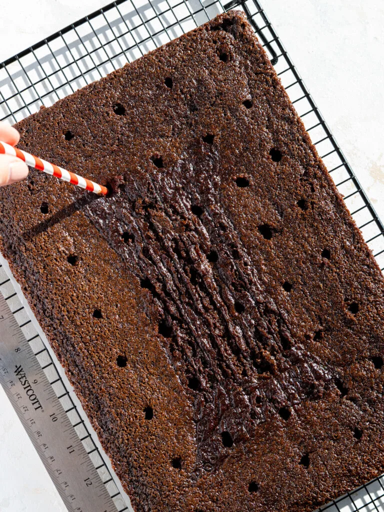 image of holes being poked into a chocolate sheet cake with a paper straw