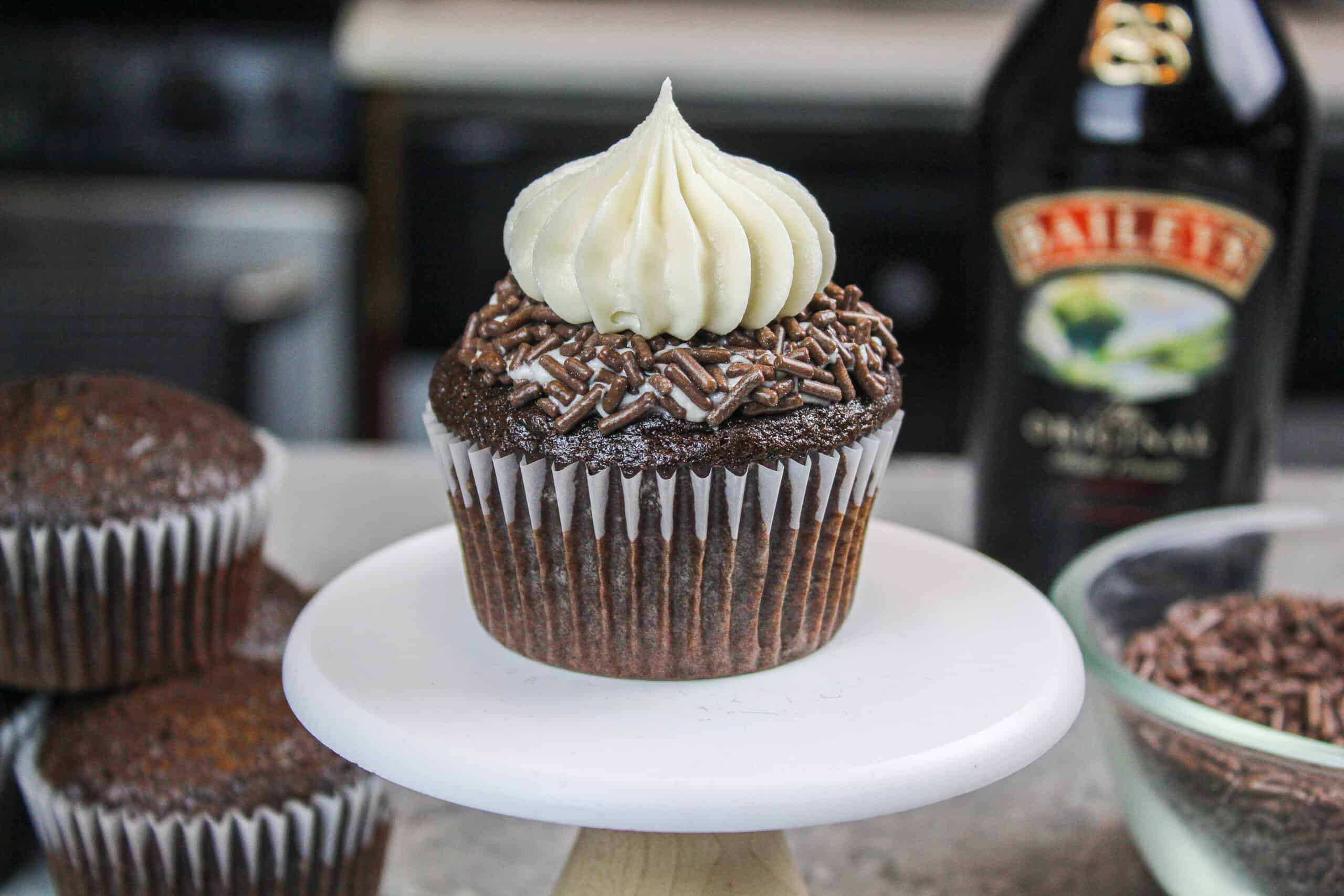 photo of a baileys chocolate cupcake on a small cupcake stand, decorated with chocolate sprinkles