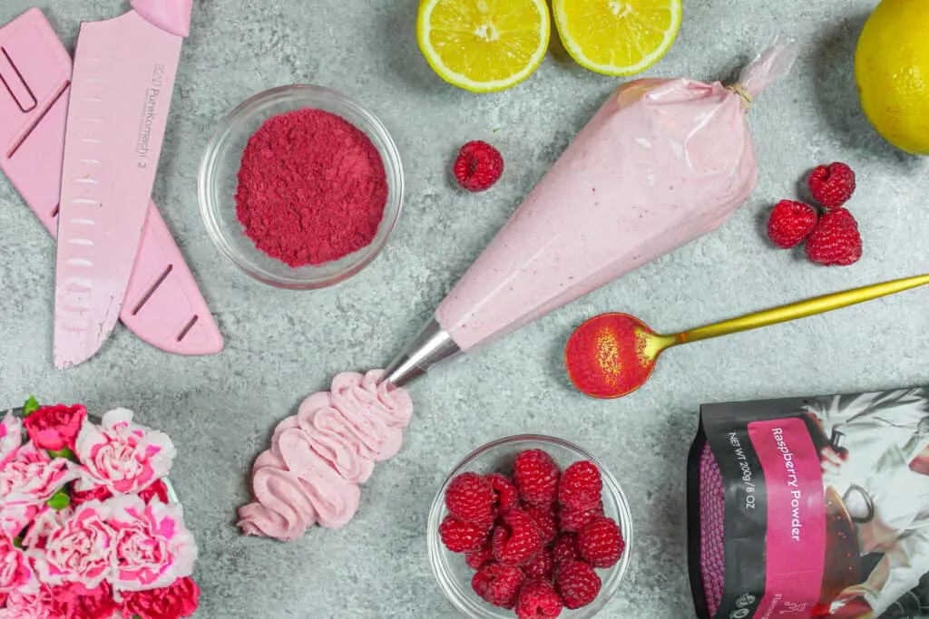 image of raspberry frosting piped into a squiggle surrounded by the ingredients used in the frosting including raspberry powder