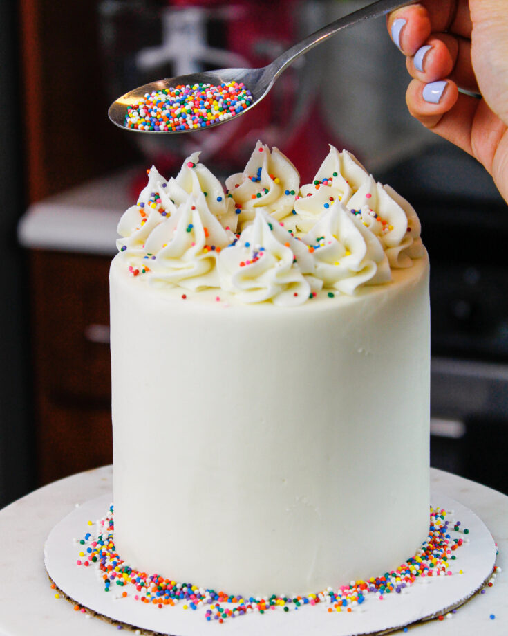 image of mini vanilla cake being decorated with rainbow sprinkles for a birthday