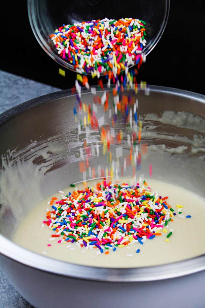 image of vegan sprinkles being poured into a vegan vanilla cake also known as a wacky cake