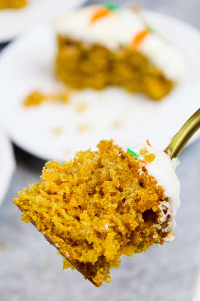 image of a bite of carrot cake on a fork with the slice behind it