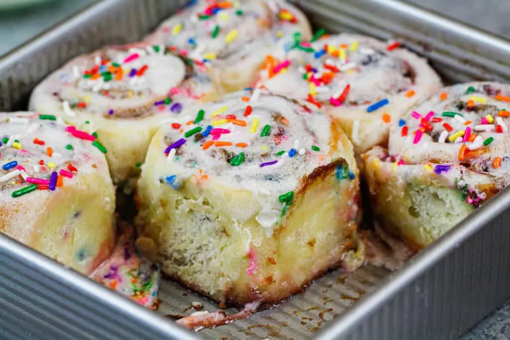 image of funfetti cinnamon rolls in a pan topped with sprinkles and vanilla icing