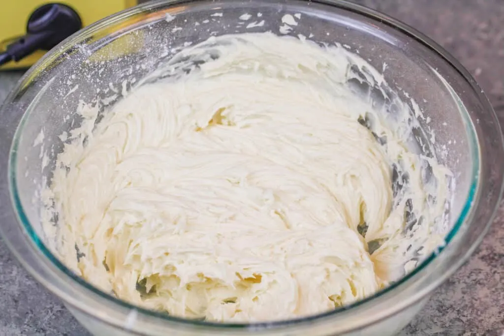 image of american buttercream frosting whipped up in a bowl to top cinnamon rolls