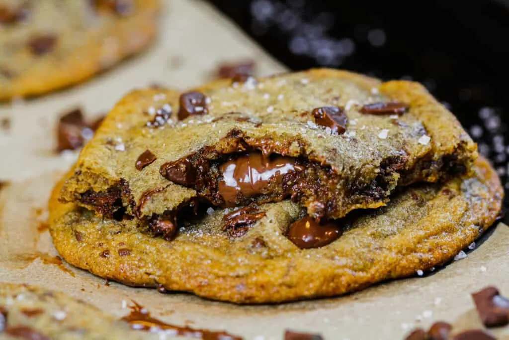 image of brown butter nutella stuffed chocolate chip cookies, with the top cookie bitten into with nutella oozing out