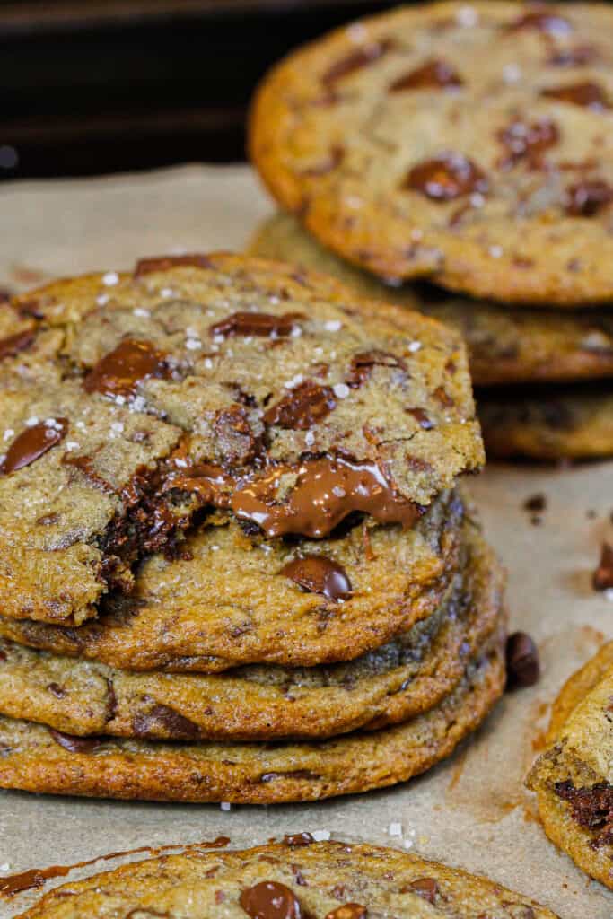 image of stack of brown butter nutella stuffed chocolate chip cookies, with the top cookie bitten into with nutella oozing out