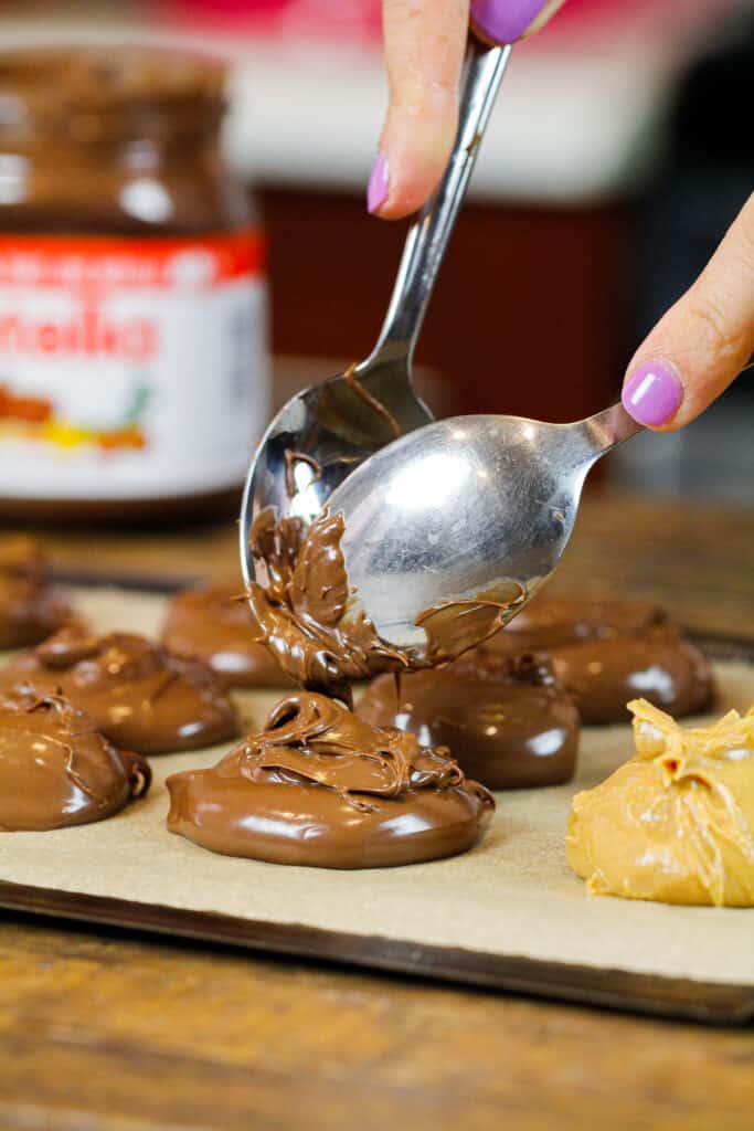 image of nutella being scooped onto a lined pan to chill before being used to fill cookies