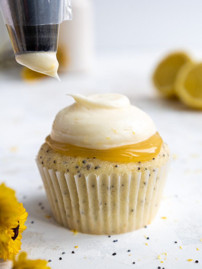 image of lemon poppy seed cupcakes being frosted with lemon cream cheese frosting using a large round piping tip