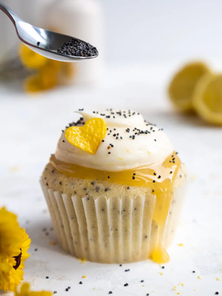 image of poppy seeds being sprinkled on top of a lemon poppy seed cupcake with a small spoon