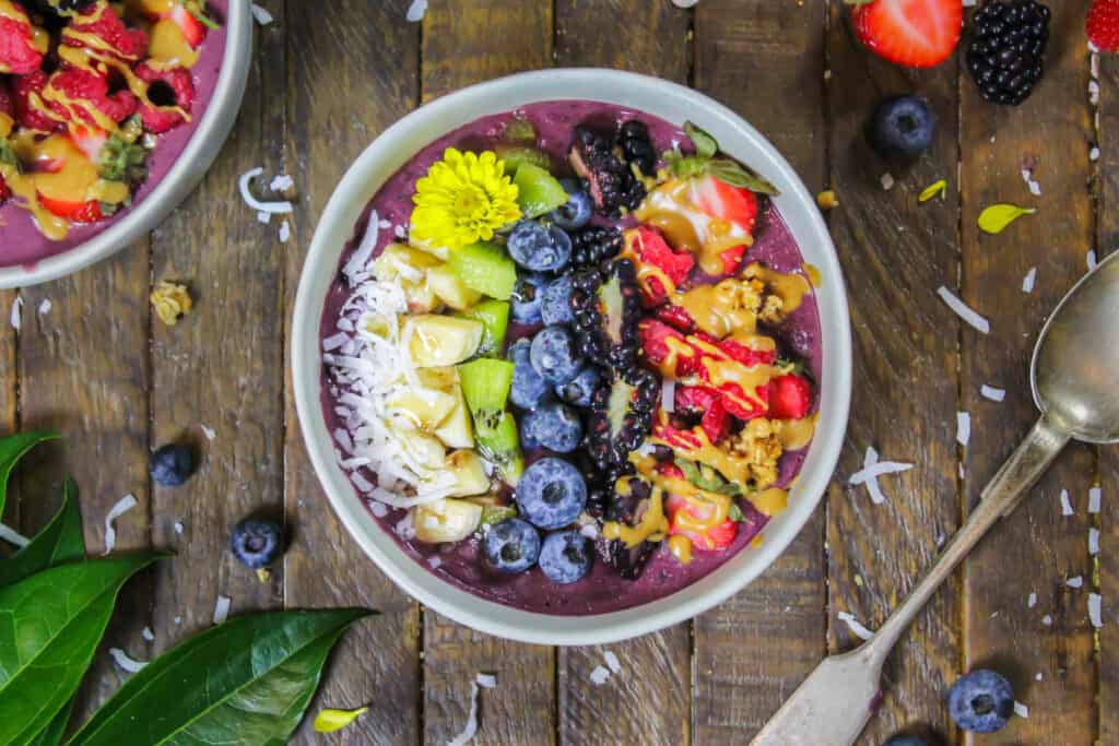 image of pretty peanut butter acai bowl decorate with fresh fruit, granola, and some edible flowers