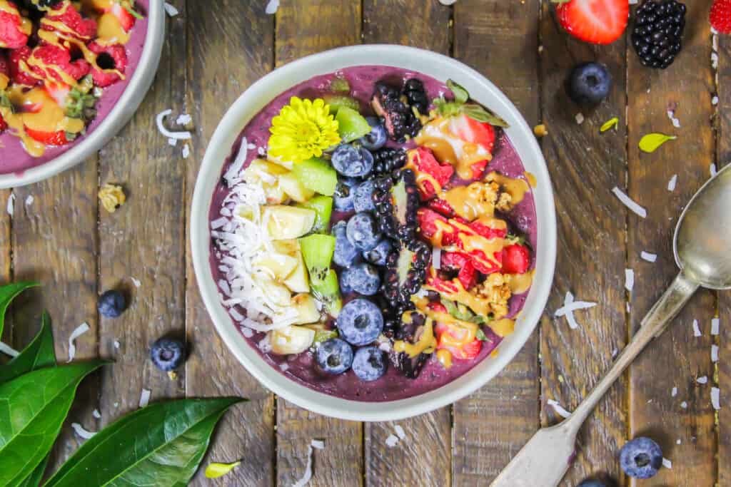 image of pretty peanut butter acai bowl decorate with fresh fruit, granola, and some edible flowers