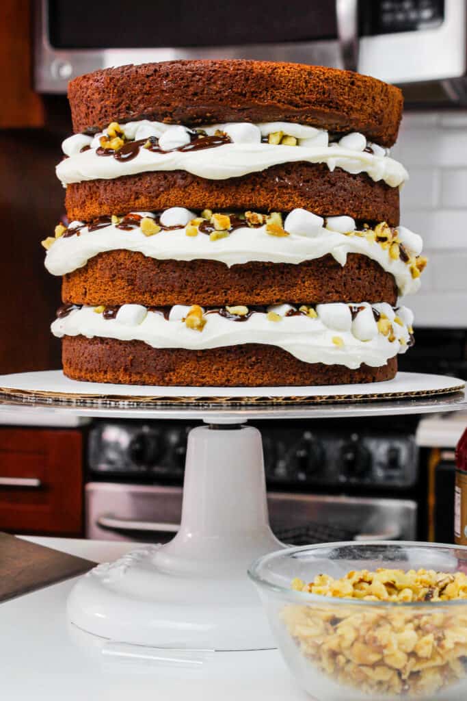 image of stacked chocolate cake layers filled with marshmallow buttercream, chocolate ganache, mini marshmallows, and chopped walnuts to make a rocky road cake