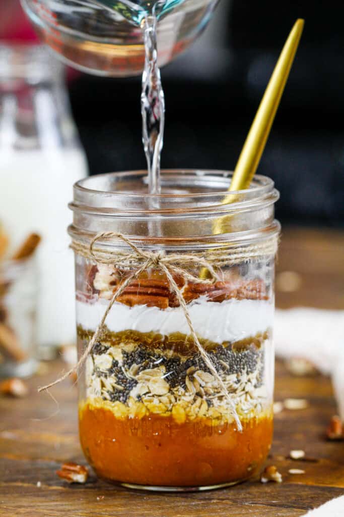 image of pumpkin spice overnight oat ingredients in a mason jar being filled with water.