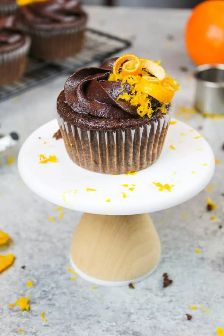 image of a chocolate orange cupcake on a little cupcake stand decorated with fresh orange zest and an orange peel spiral