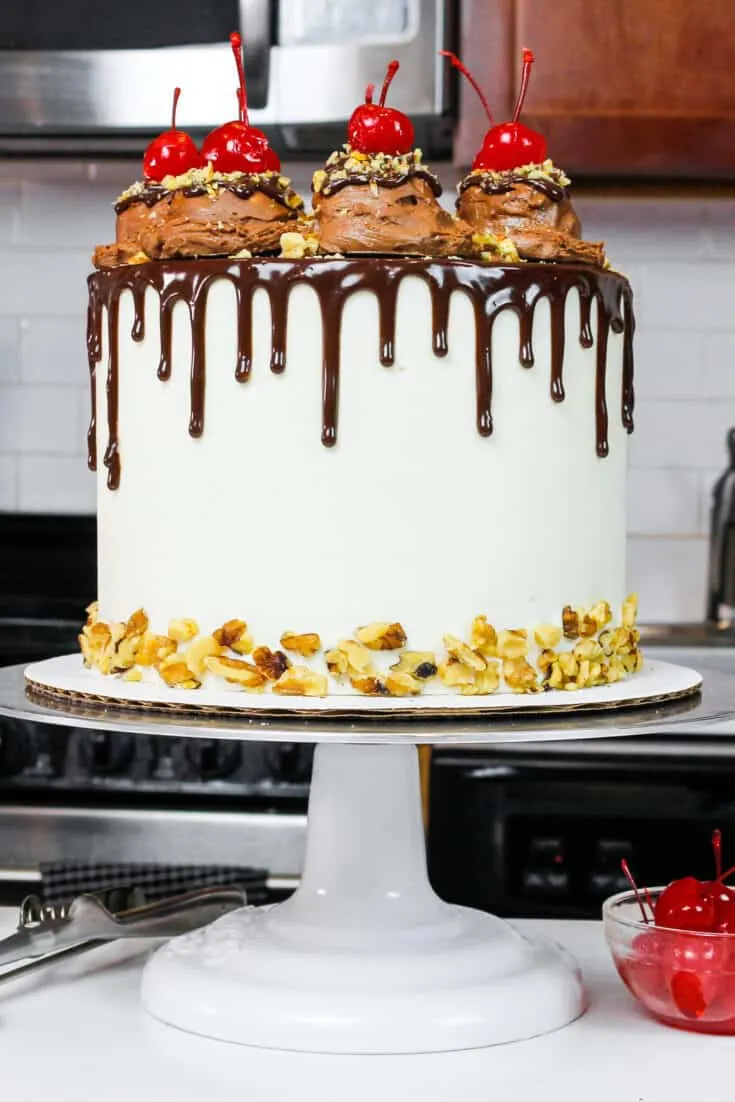 image of a rocky road cake made with fluffy chocolate cake layers, marshmallow frosting, and decorate with ice cream scoops and a chocolate drip