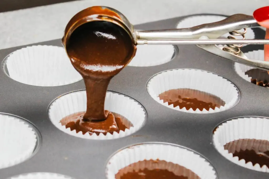 image of chocolate cupcake batter being scooped into a cupcake liner