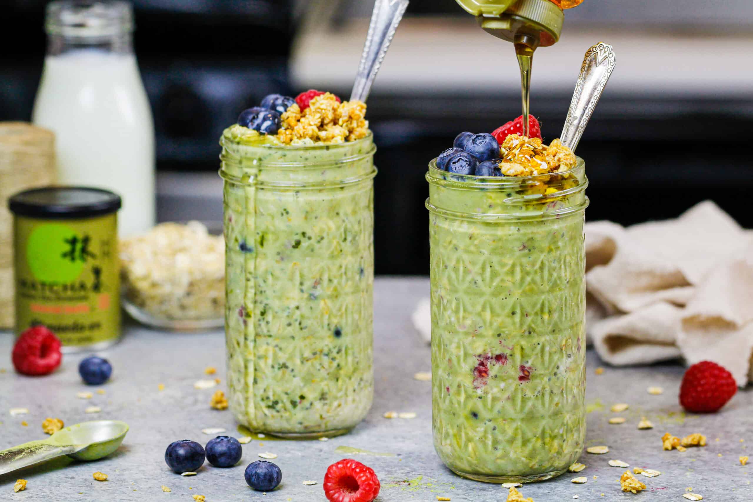 image of matcha overnight oats in cute mason jars topped with raspberries, blueberries and honey
