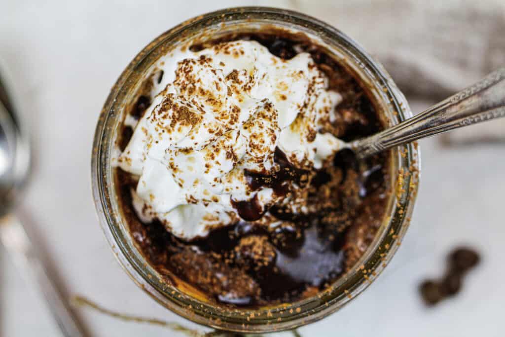image of a mason jar of overnight oats shot from overhead to show the whipped cream and chocolate syrup topping