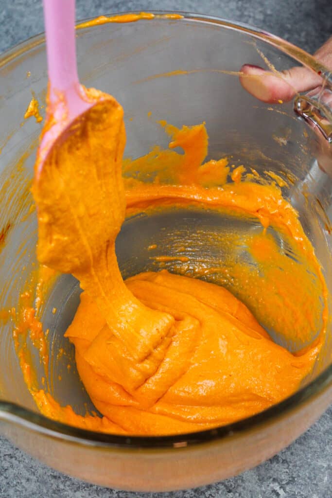 image of orange macaron batter that's been mixed properly and falls of a spatula in thick ribbon that has a lava-like consistency