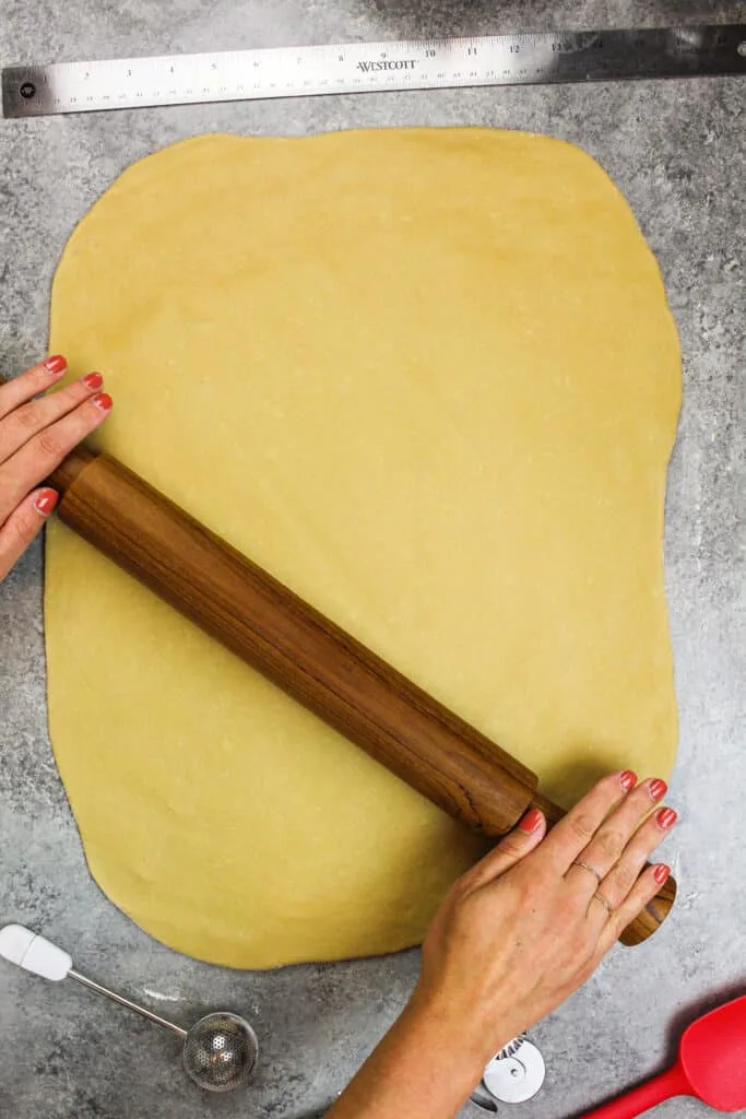 image of cinnamon roll dough being rolled out on a floured surface.