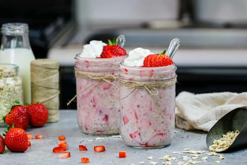 image of strawberry overnight oats made in cute mason jars and topped with a dollop of whipped cream and sliced strawberries
