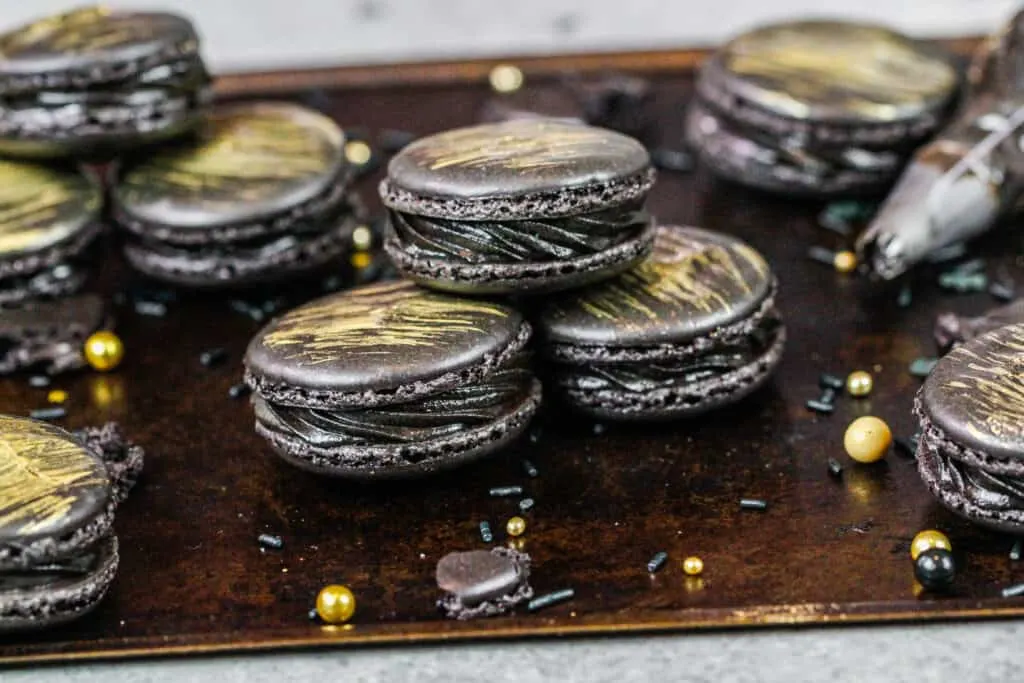 image of french black macarons that have been filled with black frosting and brushed with a beautiful gold streak of edible gold paint