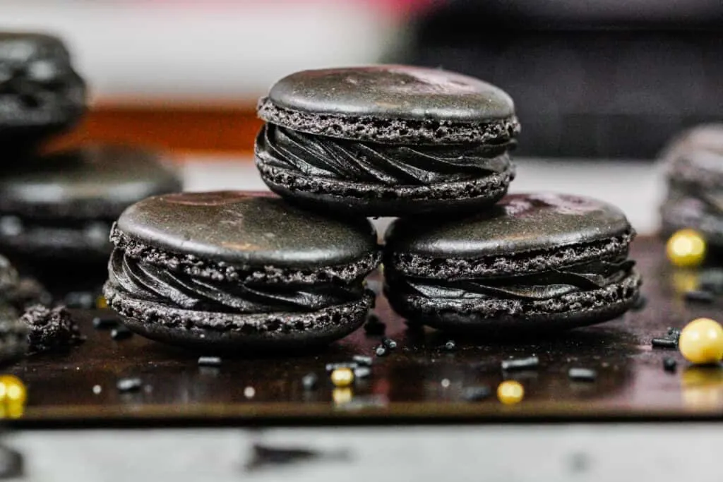 image of black macarons stacked on a baking tray to show their black chocolate frosting