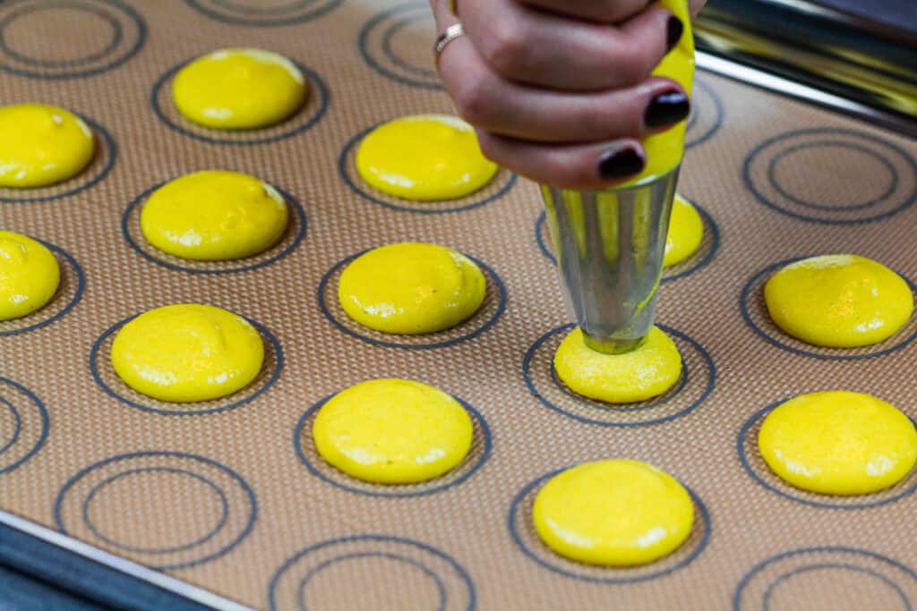 image of yellow macaron shells being piped onto a silpat mat