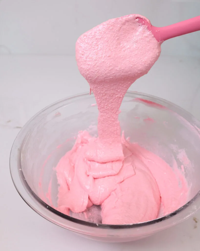 image of pink macaron batter that's been mixed perfectly and is flowing in thick ribbons. This helps prevent hollow macarons.
