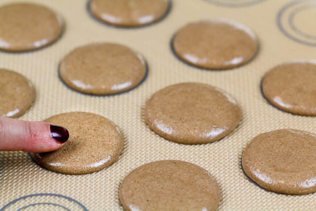 image of chocolate macarons piped on a silicon mat and resting to form a skin before being baked