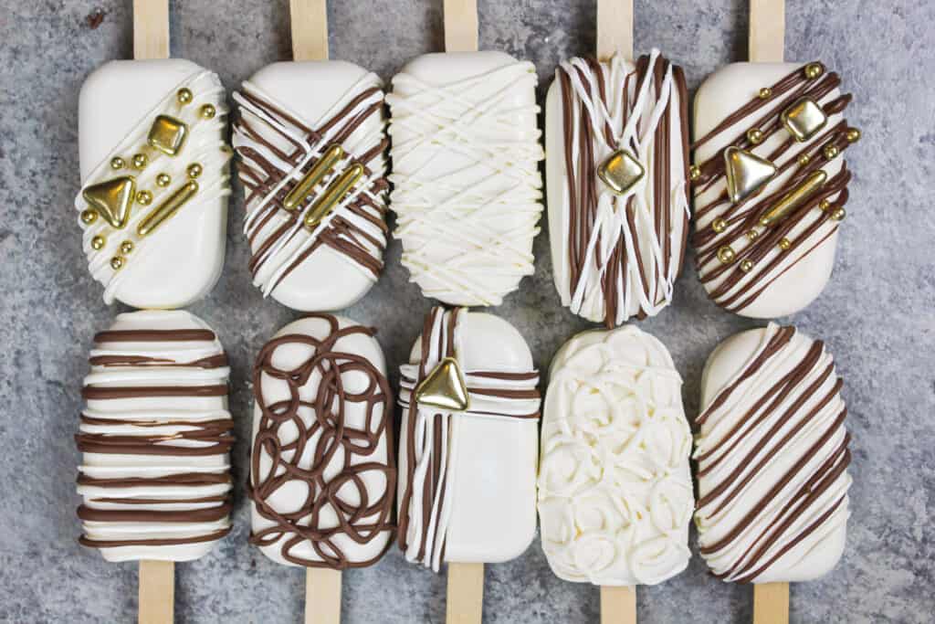 image of cakesicles decorated with white and dark chocolate drizzles and pretty gold sprinkles