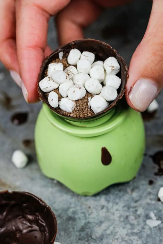 image of a chocolate sphere being filled with hot cocoa mix and marshmallows to make a hot cocoa bomb