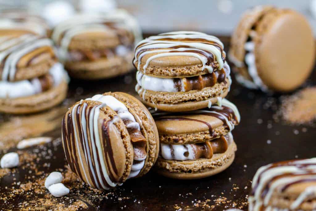 image of hot cocoa macarons filled with hot cocoa and marshmallow buttercream that are stacked a tray surrounded be mini marshmallows