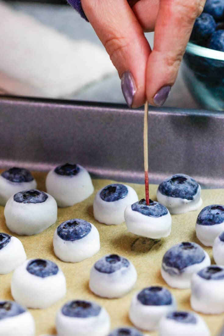 image of frozen yogurt blueberries being dipped and placed on a baking sheet