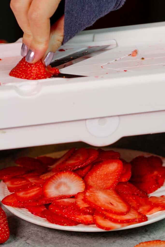 image of a strawberry being sliced on a mandolin to make dried strawberries