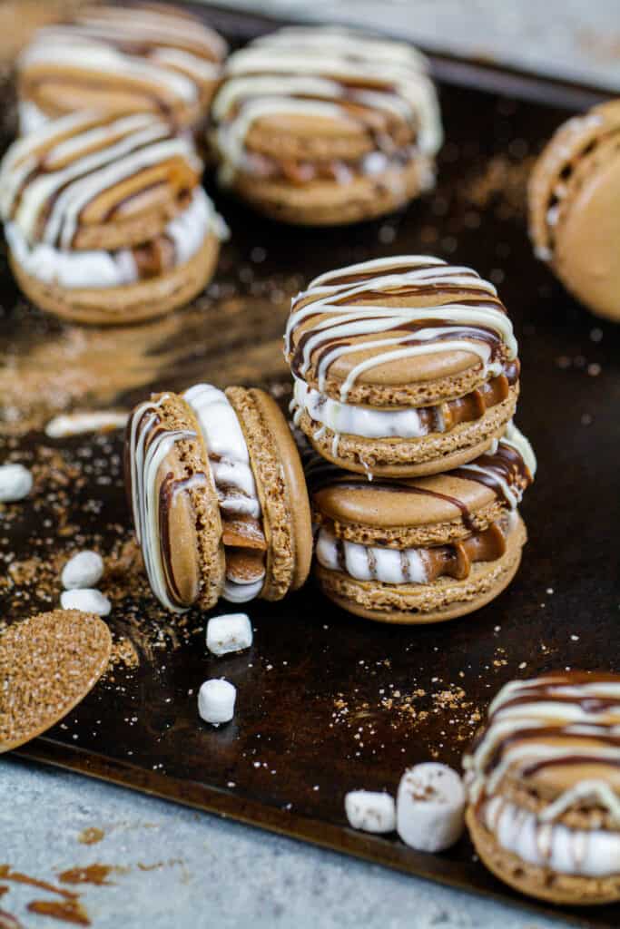 image of hot cocoa macarons filled with hot cocoa and marshmallow buttercream that are stacked a tray surrounded be mini marshmallows