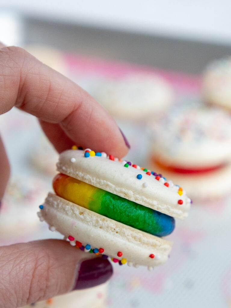 image of a rainbow frosting macaron being held up to show it's colorful filling