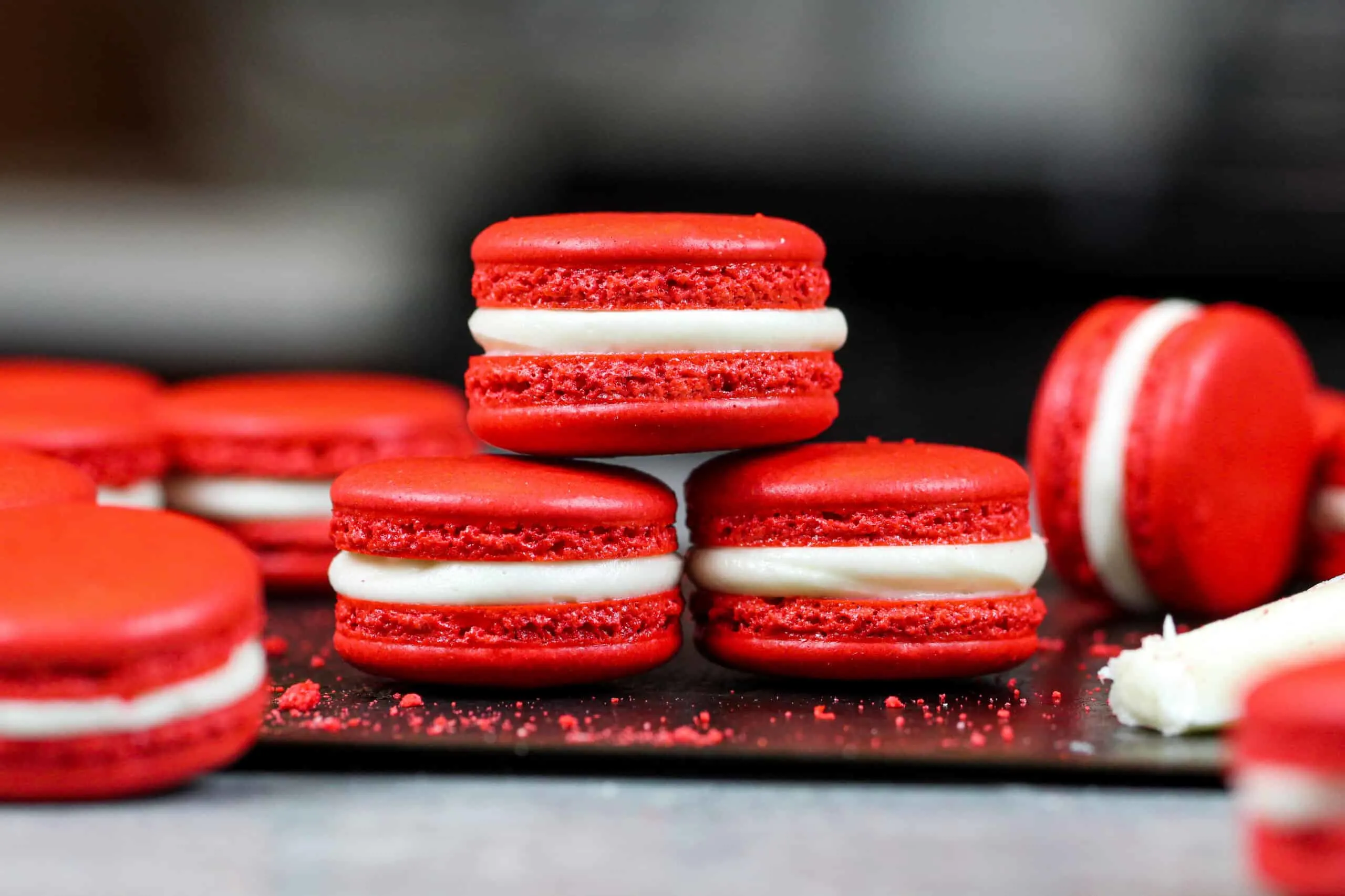 image of red velvet macarons filled with cream cheese frosting that are stacked on each other to show their perfect feet