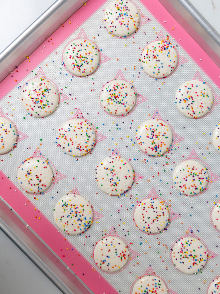 image of white macaron shells that are sprinkled with nonpareil sprinkles and have rested and now look matte