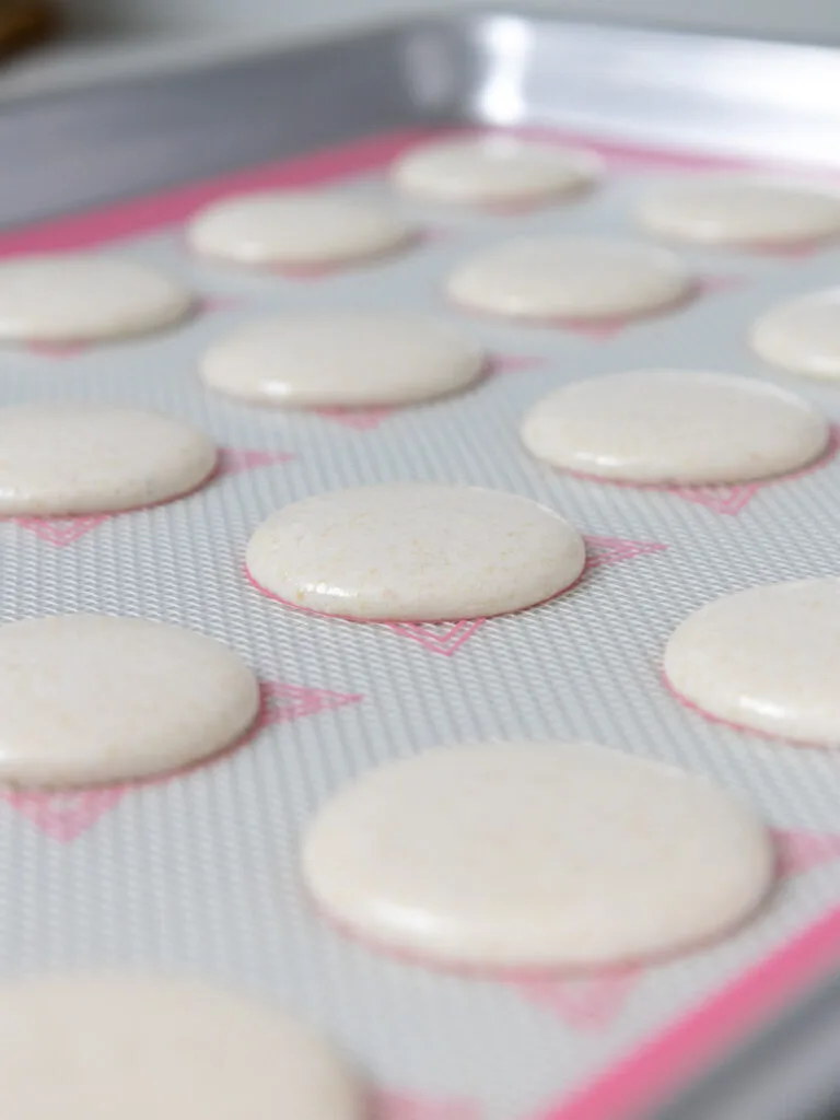 image of white macaron shells that have been piped on a silpat mat