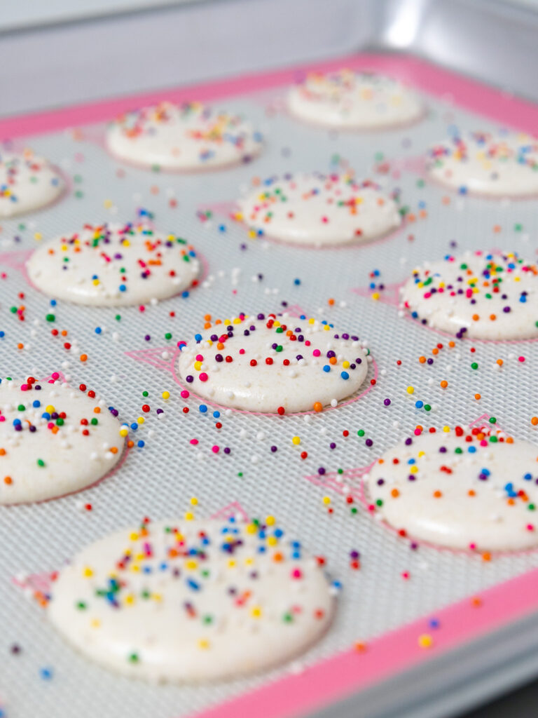 image of white macaron shells that have been sprinkled with rainbow nonpareil sprinkles
