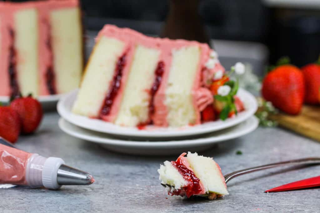 image of a slice of vanilla strawberry cake filled with strawberry jam and strawberry frosting