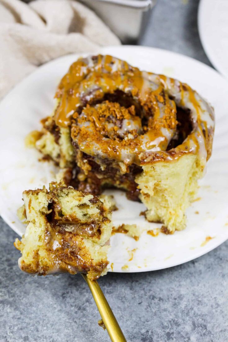image of a biscoff cookie butter cinnamon roll on a plate that's been cut into to show how fluffy and soft it is