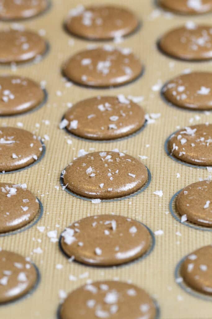 image of chocolate macaron shells that have been sprinkled with sea salt to make salted caramel macarons