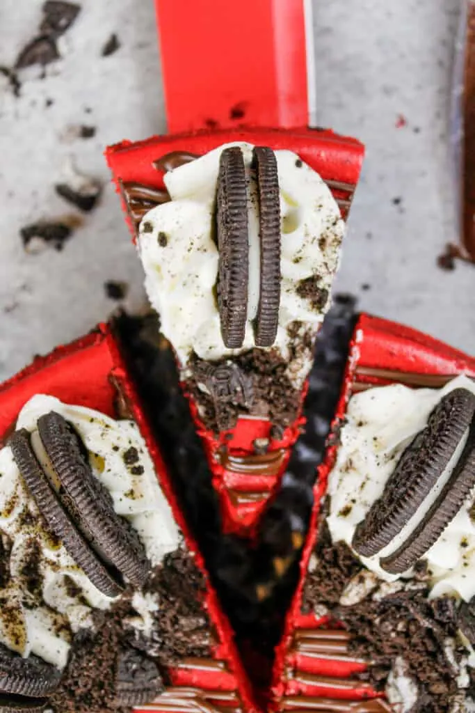 image of red velvet oreo cheesecake that's been cut and is having a slice pulled out to be eaten